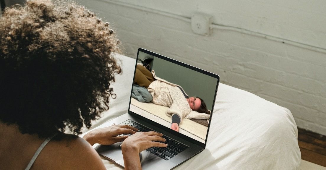 Een vrouw ligt op een bed en kijkt op een laptop naar een yogales.