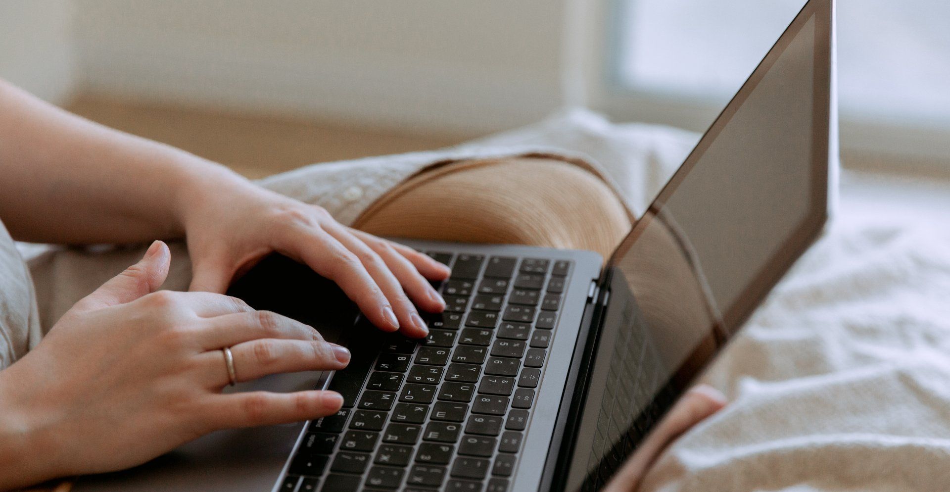 Een vrouw zit op bed en gebruikt een laptop.