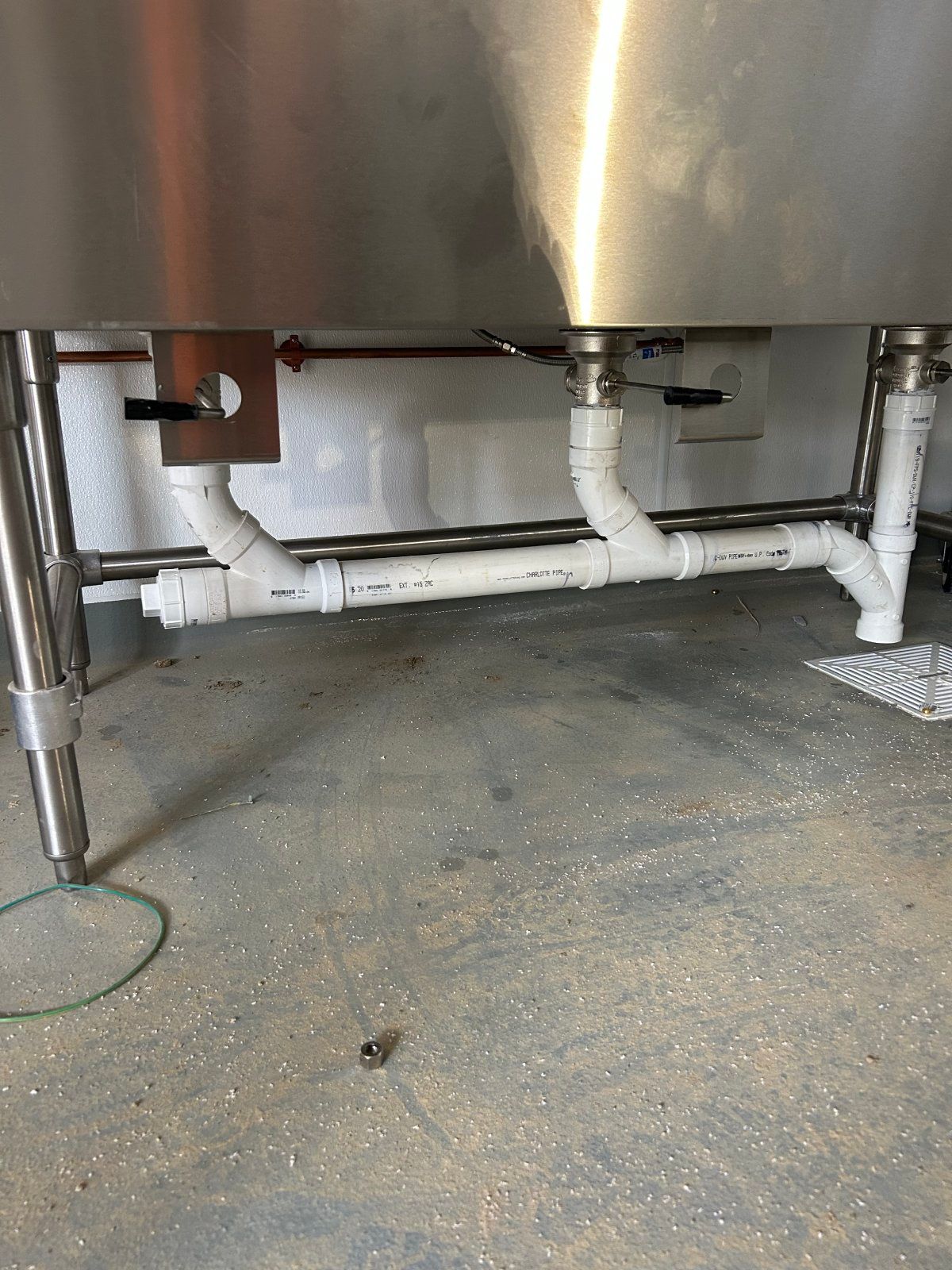 White PVC plumbing pipes connect underneath a stainless steel sink in a professional kitchen.