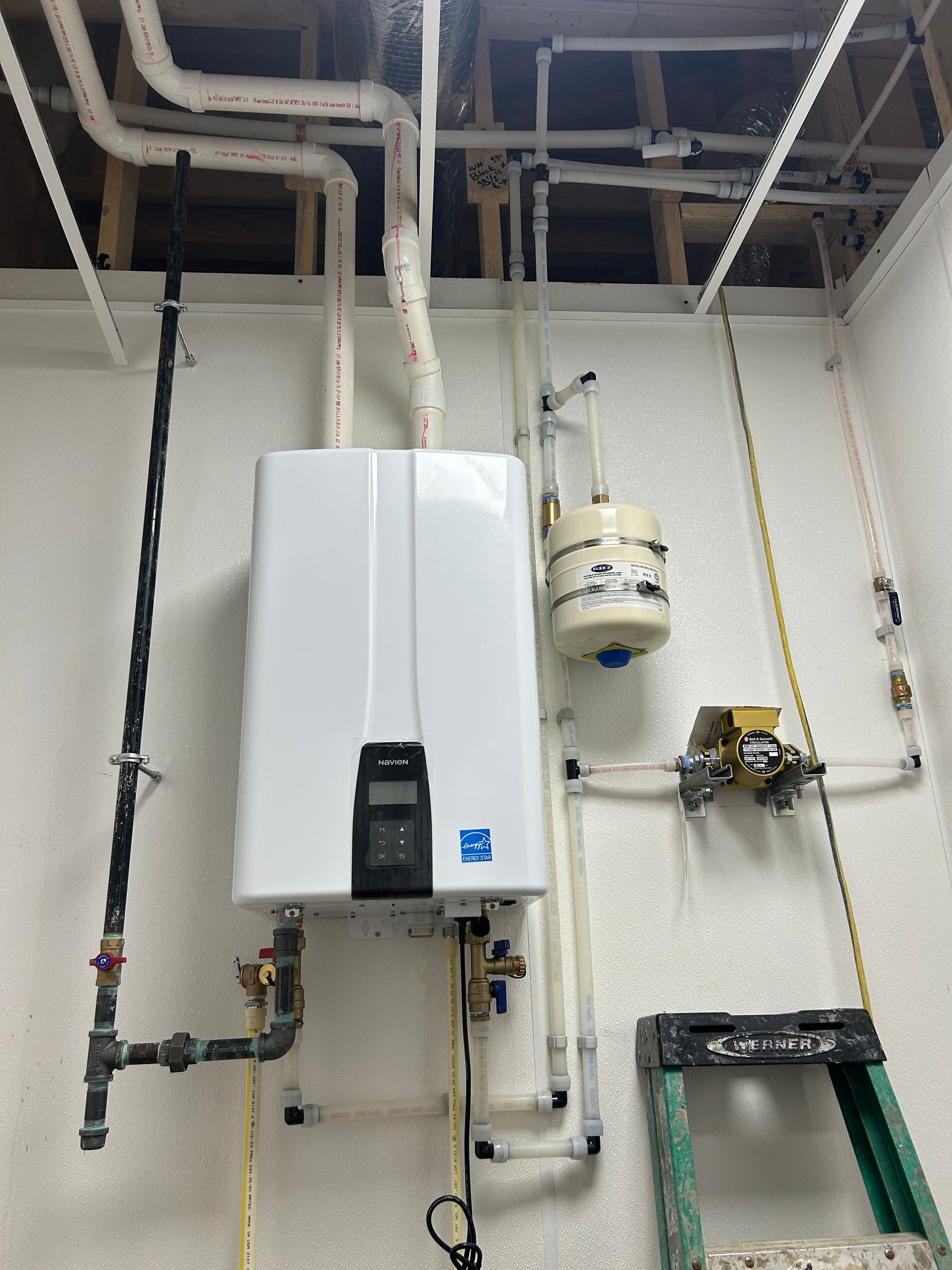 Wall-mounted tankless water heater with plumbing, a small expansion tank, and gas line in a utility room.