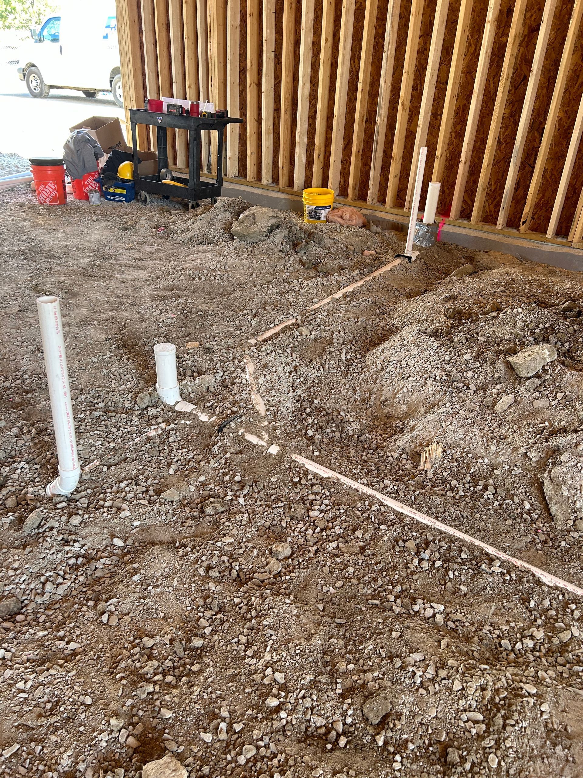 Construction site with PVC plumbing pipes installed in the ground next to a wooden fence.