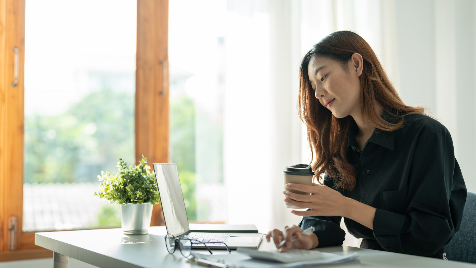 A woman is sitting at a desk with a laptop and a cup of coffee.