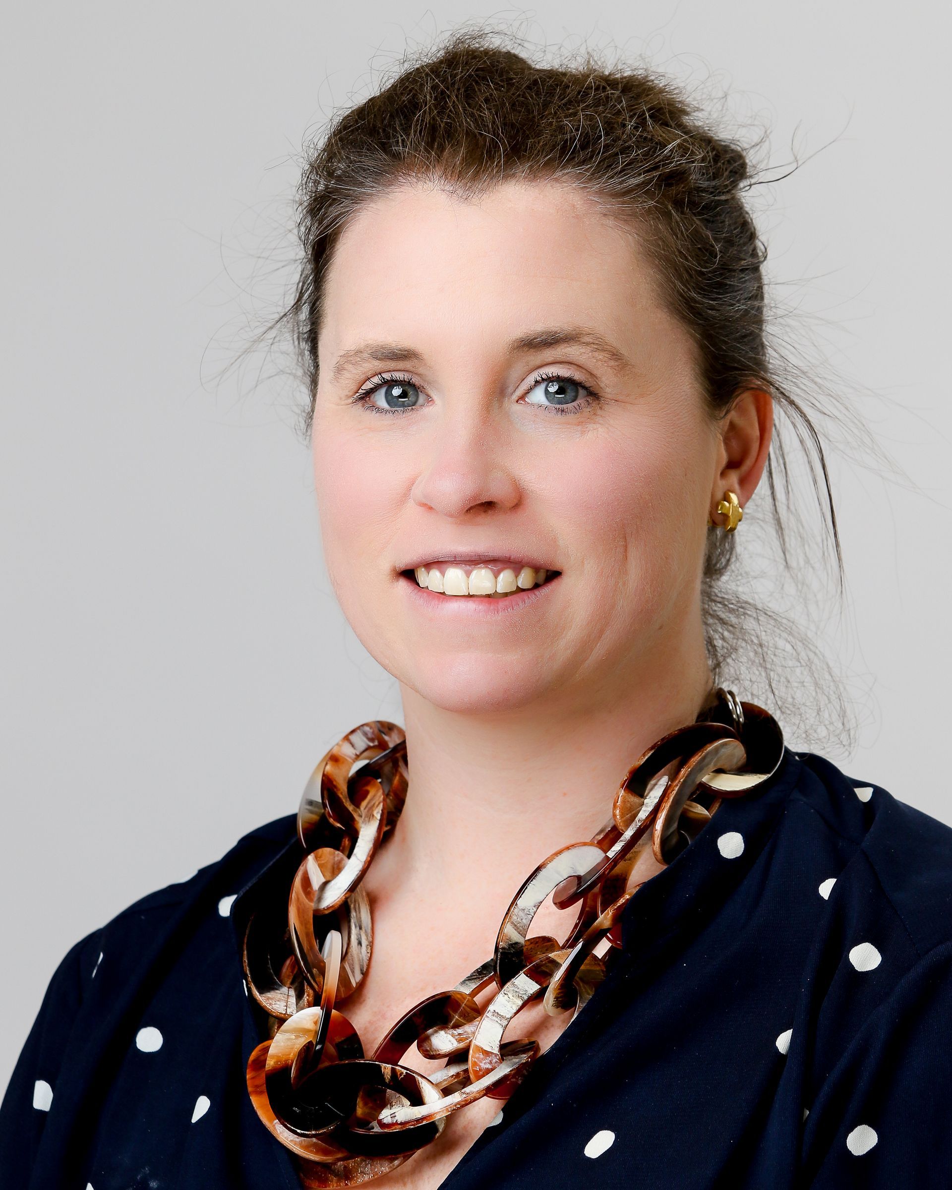 A woman wearing a polka dot shirt and a necklace smiles for the camera.
