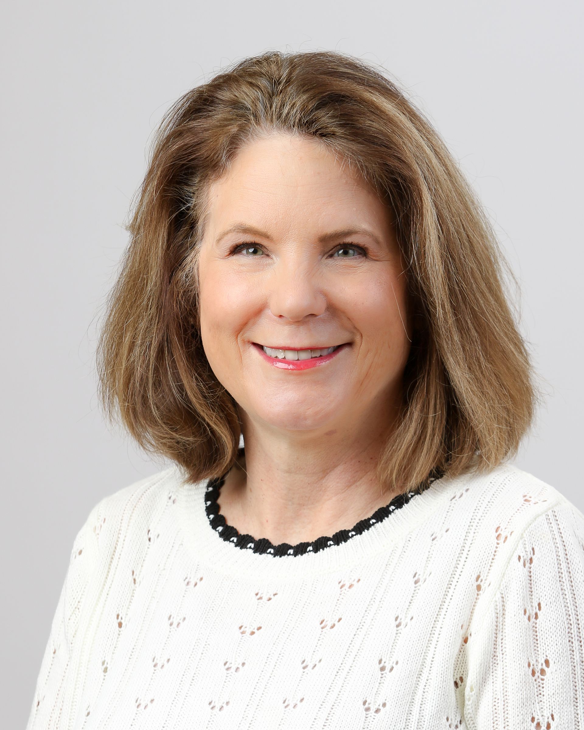 A woman is wearing a white sweater and smiling for the camera.