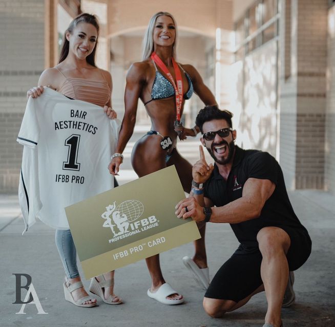 A man and two women are posing for a picture while holding a card and a shirt.
