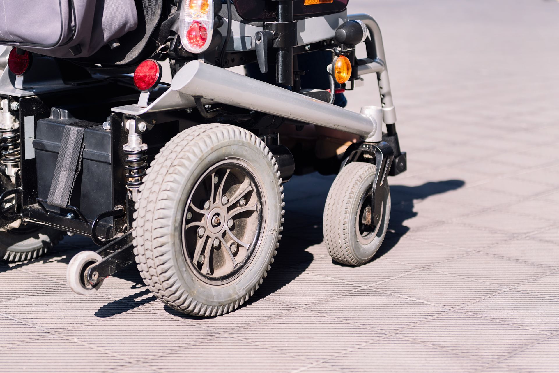Rear view of an electric power wheelchair with large drive wheels parked on a sunny sidewalk.