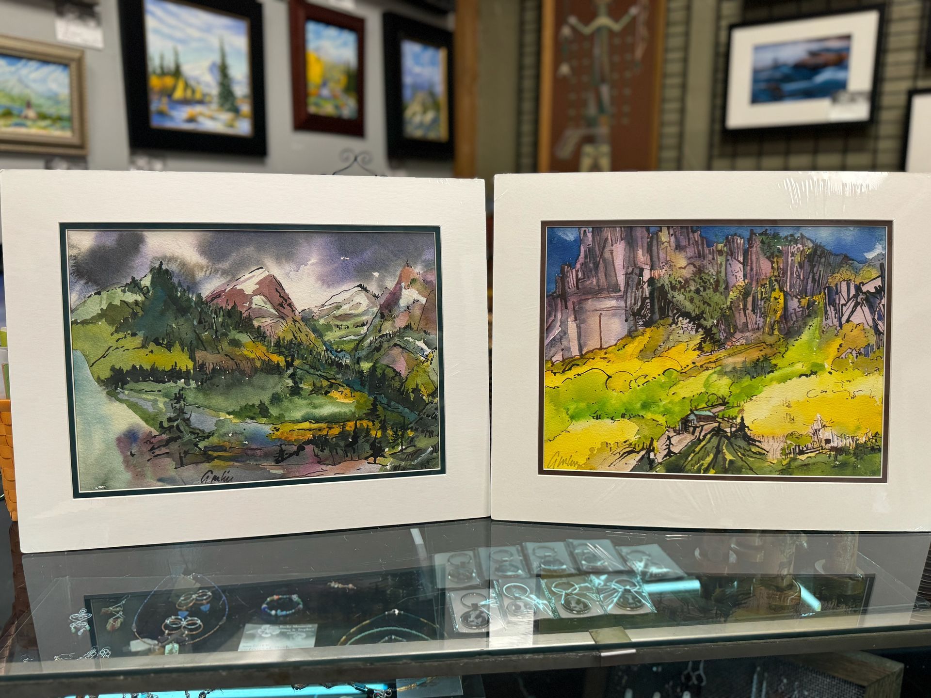 Two paintings of mountains are sitting on a glass table.