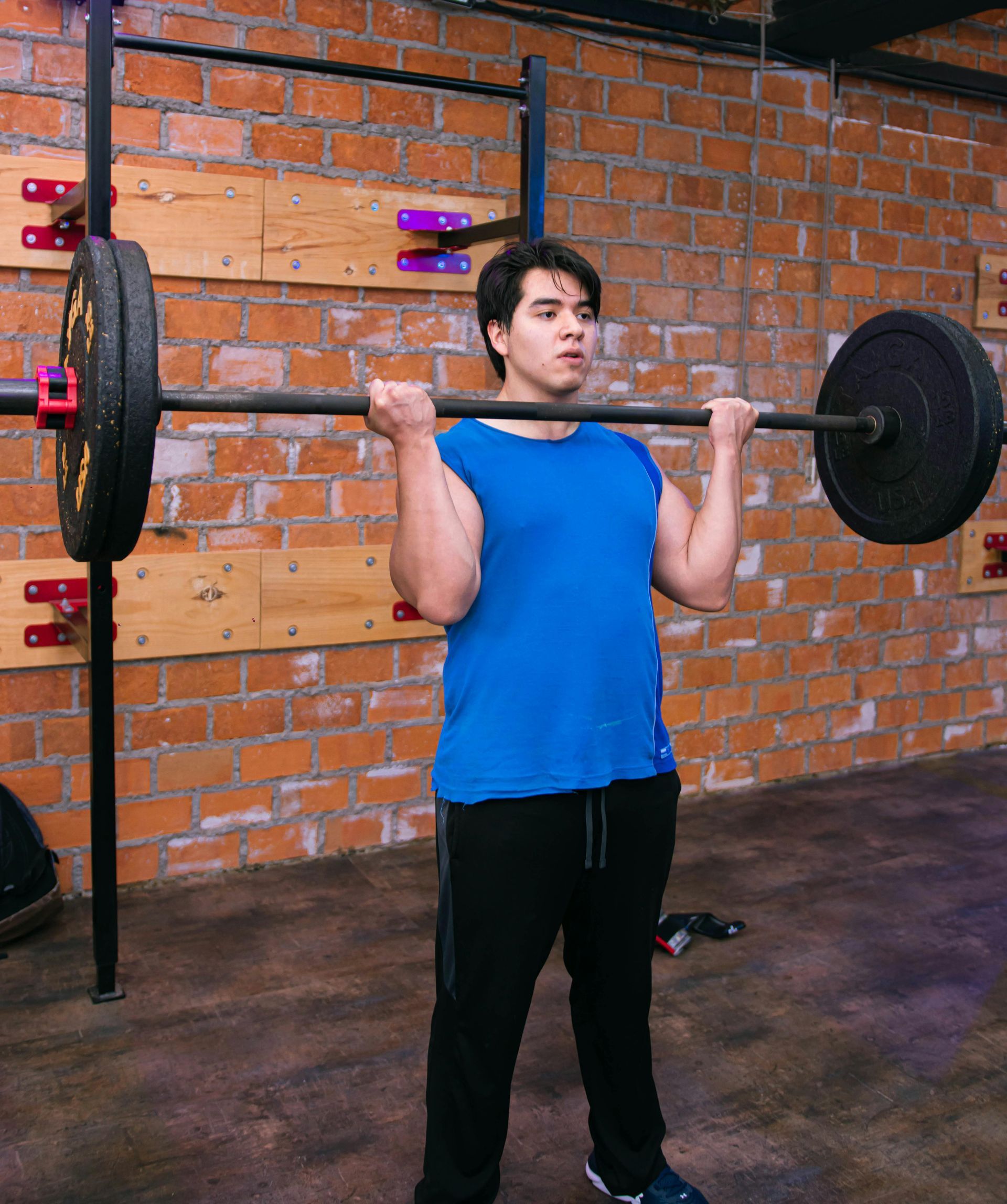 Person lifting a barbell in a gym, wearing a blue shirt and black pants.