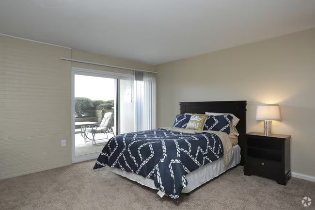 Bedroom with a navy patterned bedspread, nightstand lamp, and sliding door to a balcony.