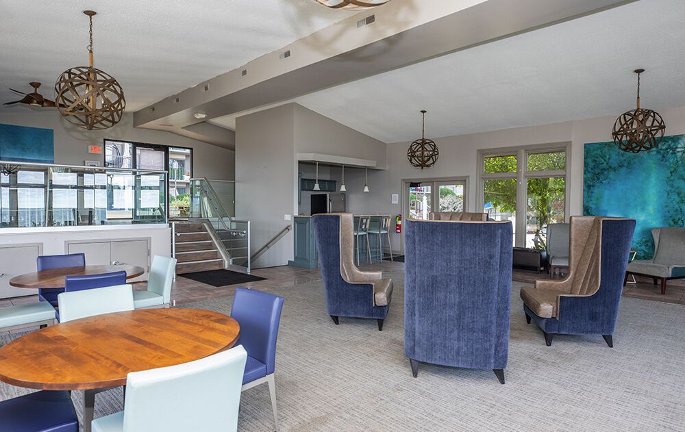 Modern lounge with blue chairs, wooden tables, and large windows in a bright open interior