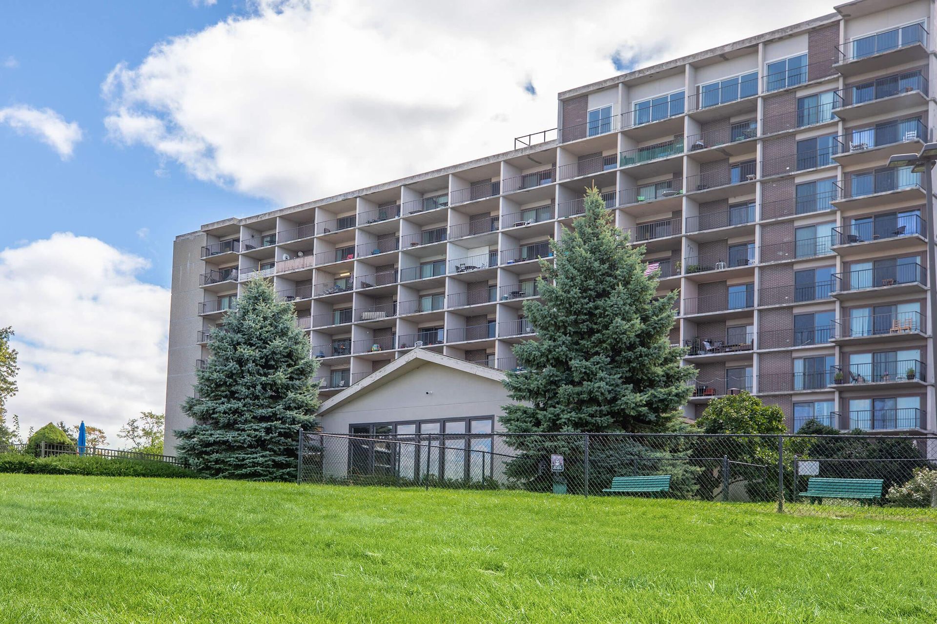 Modern apartment building with balconies behind a grassy lawn and tall evergreen trees