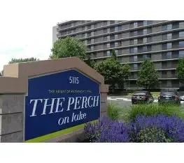Sign for The Perch on Lake apartment building with purple flowers and a modern high-rise in the background