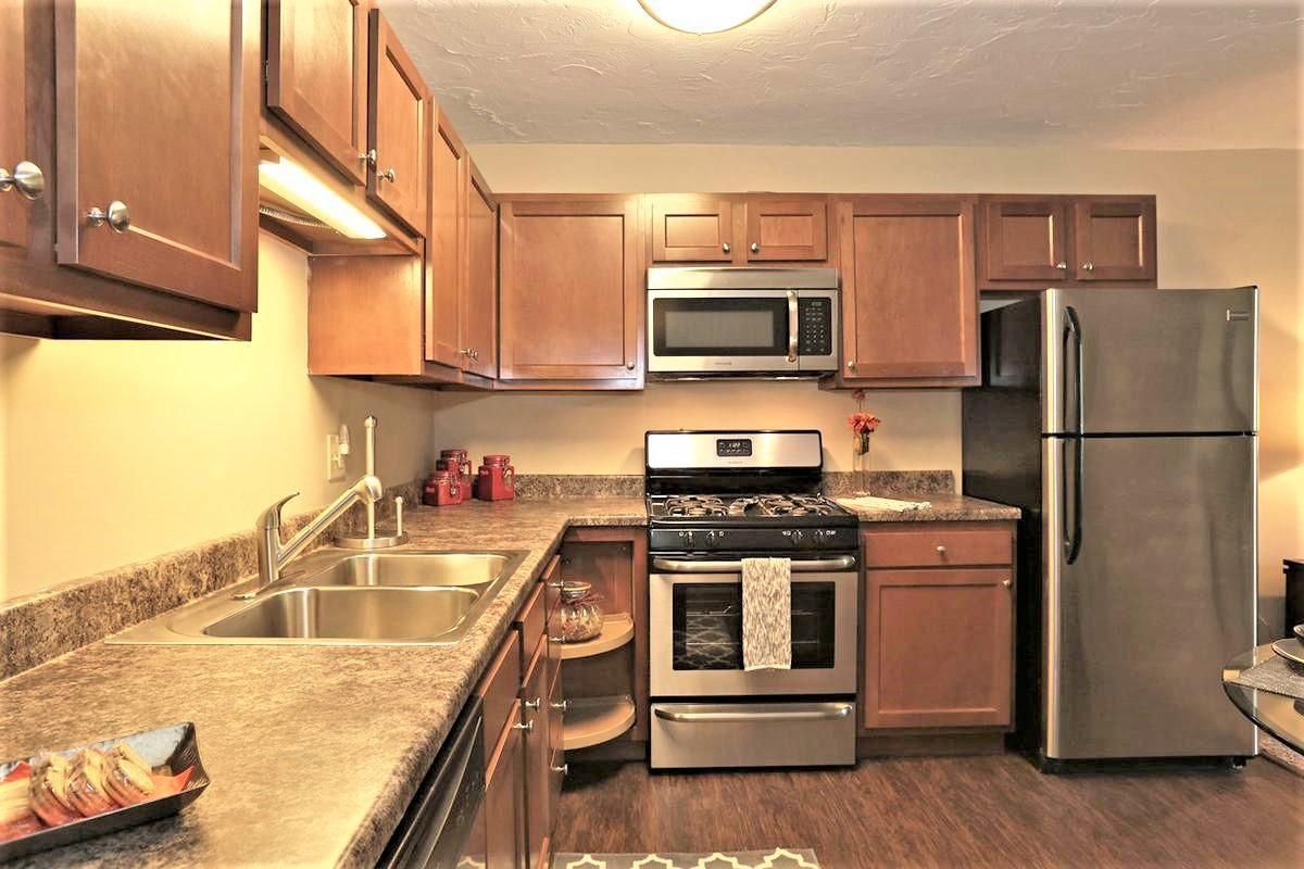 Small modern kitchen with wooden cabinets, granite counters, stainless steel appliances, and tiled backsplash
