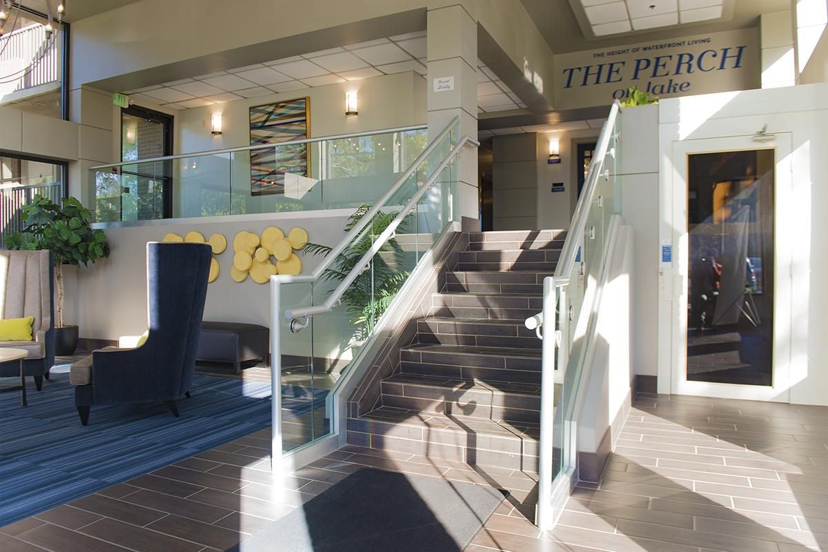Hotel lobby with staircase, glass railings, seating, and reception area.