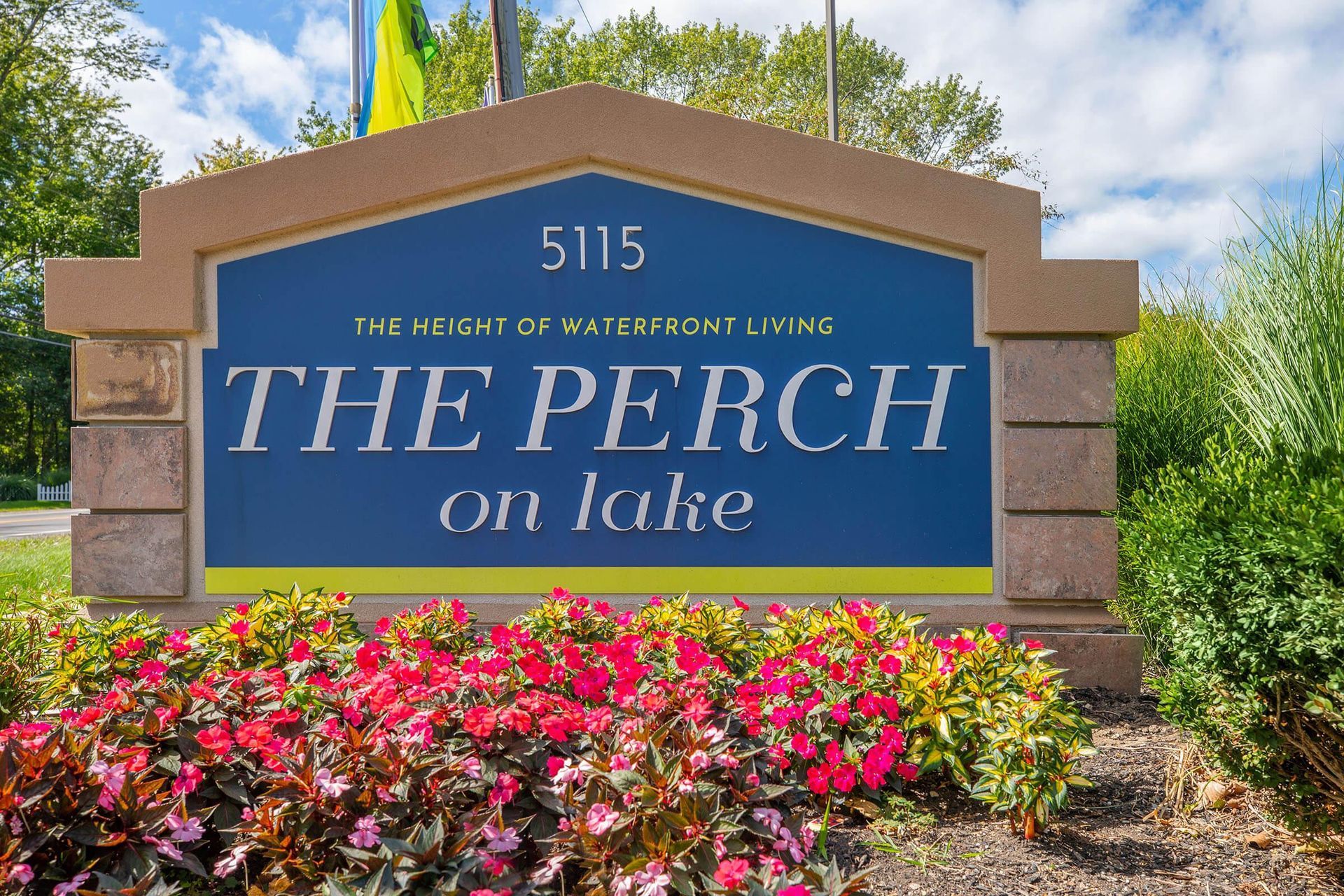 Entrance sign for The Perch on Lake, with blue lettering, stone pillars, and colorful flowers