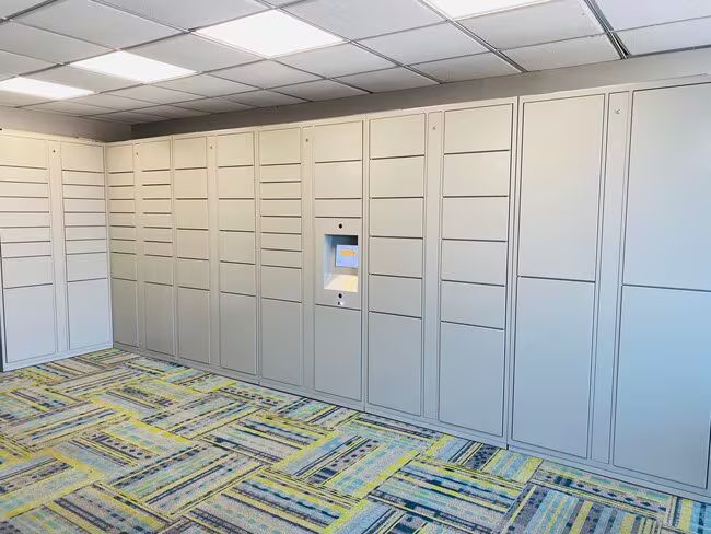Empty office with built-in wall cabinets, a small monitor inset, and patterned carpet under fluorescent ceiling lights