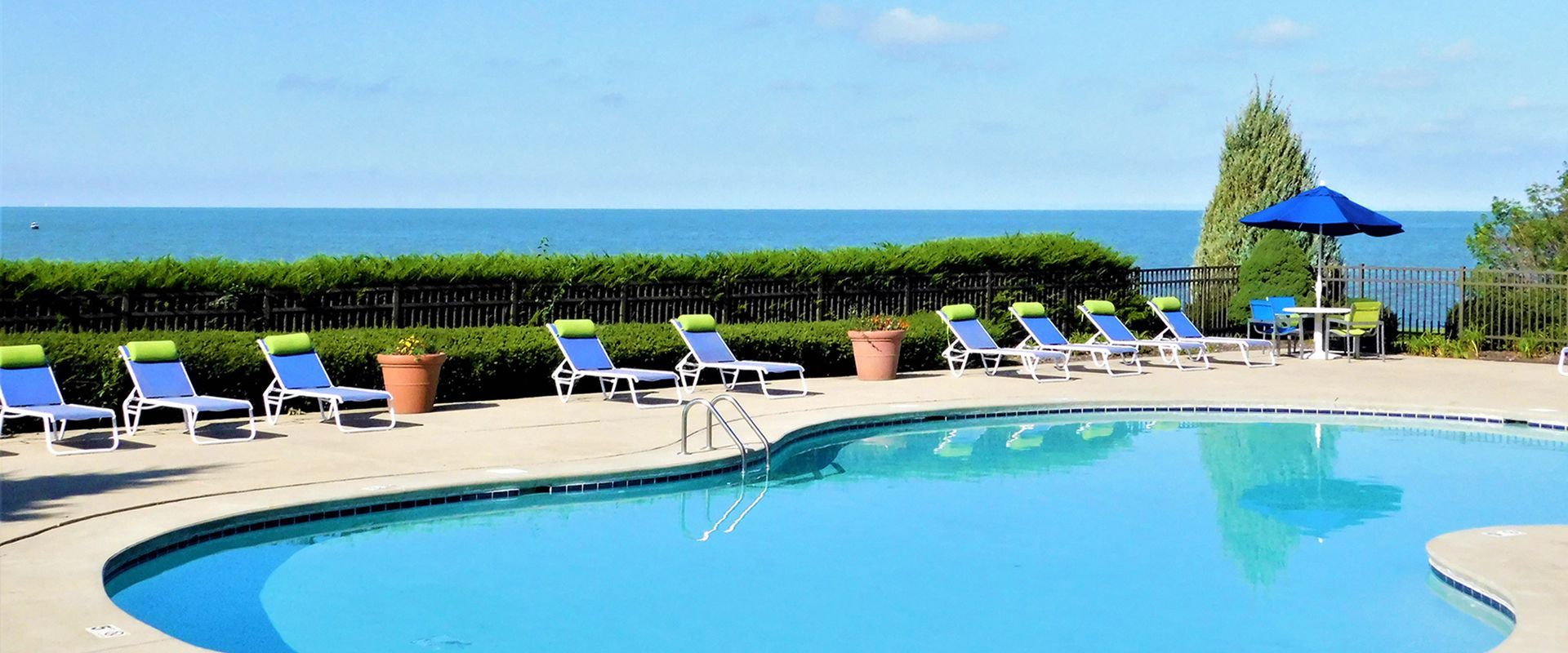 Poolside resort with blue lounge chairs, umbrellas, and a clear swimming pool overlooking the sea