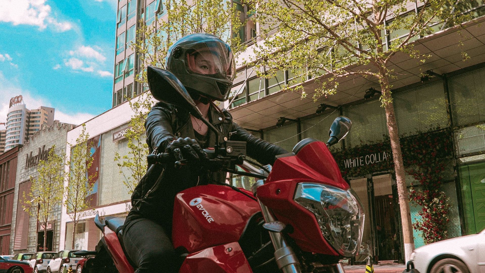 A woman is riding a red urban-s, an electric motorcycle down a city street in New York, USA 2021.
