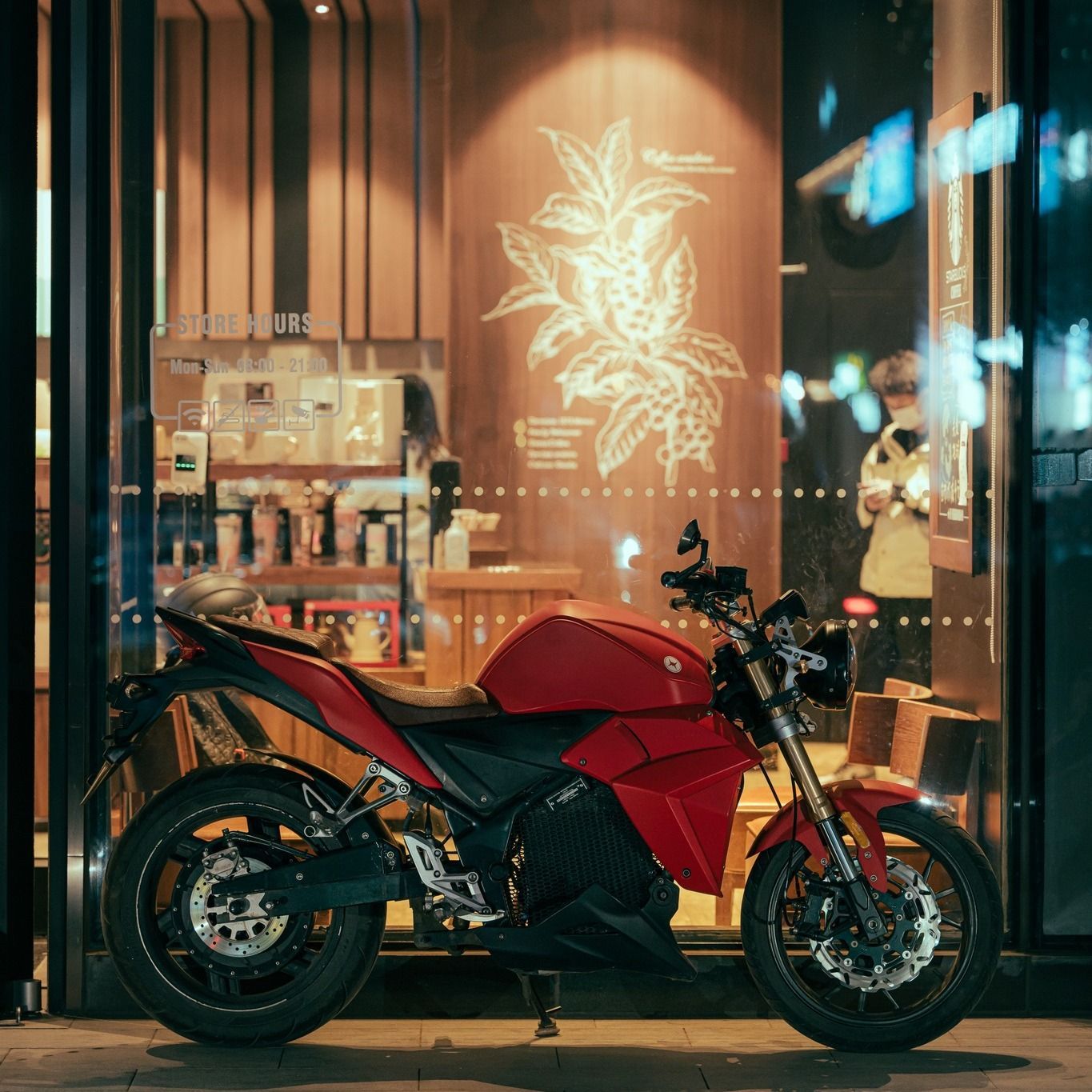 A red Urban Classic electric motorcycle is parked in front of a Starbucks window in New York 2023