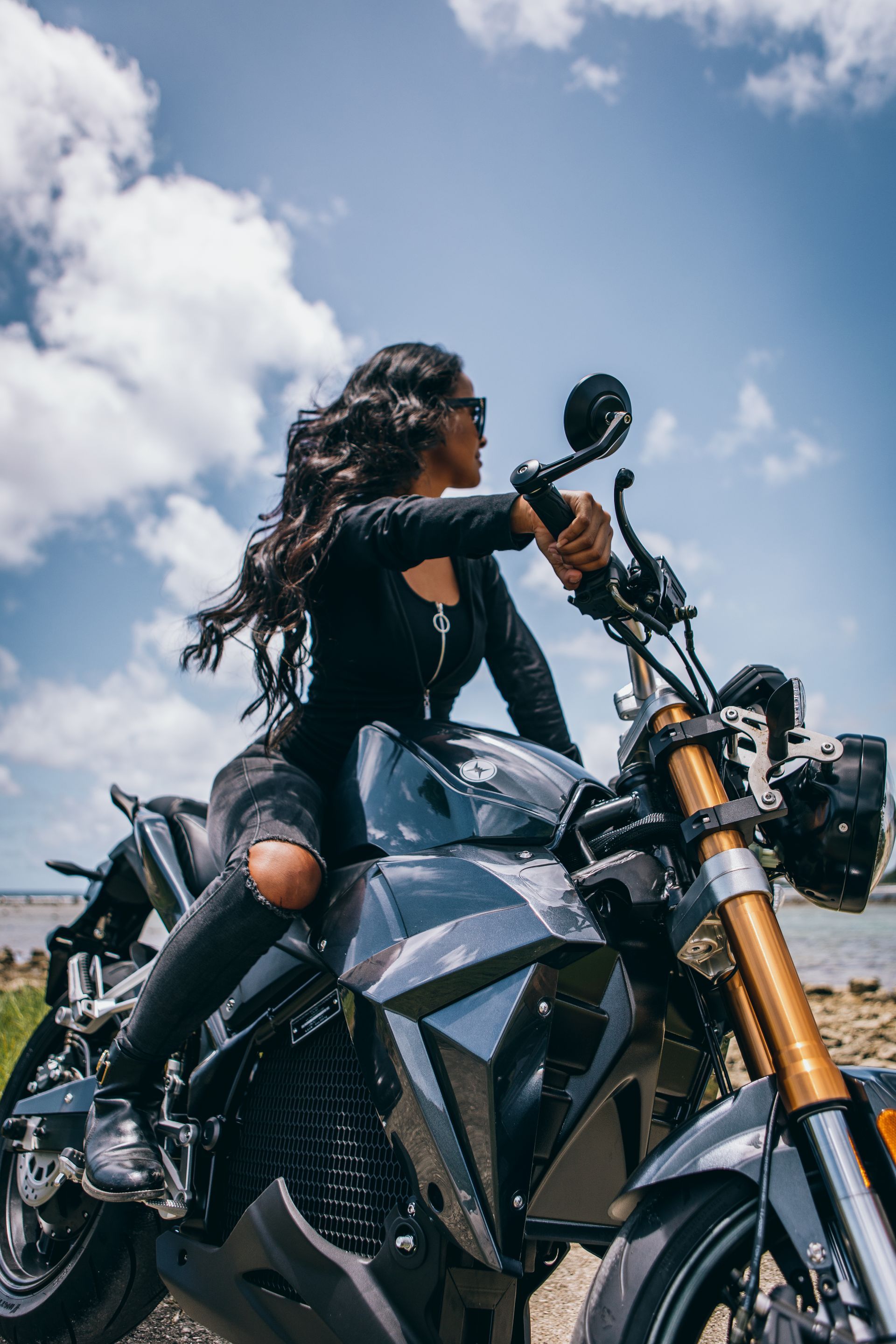 A hot woman is sitting on an electric motorcycle near the ocean. Urban Classic 2024 Guam