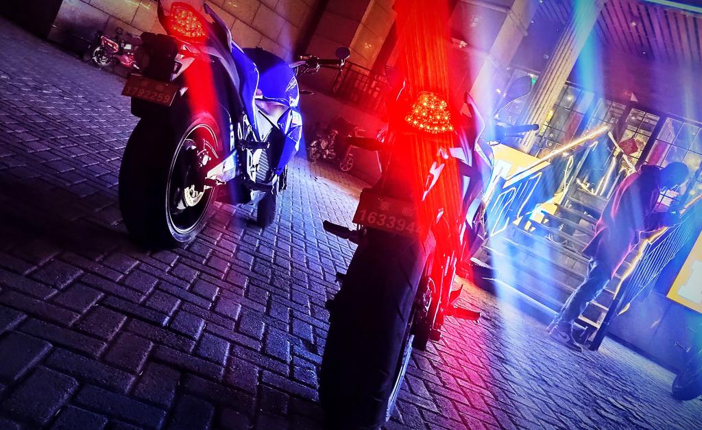 Two electric motorcycles are parked next to each other on a cobblestone street at night.