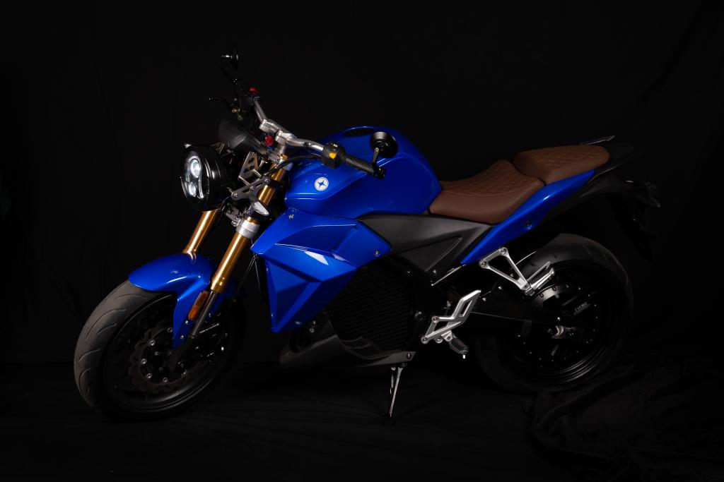 A blue electric motorcycle is parked in a dark room. Urban Classic 2024