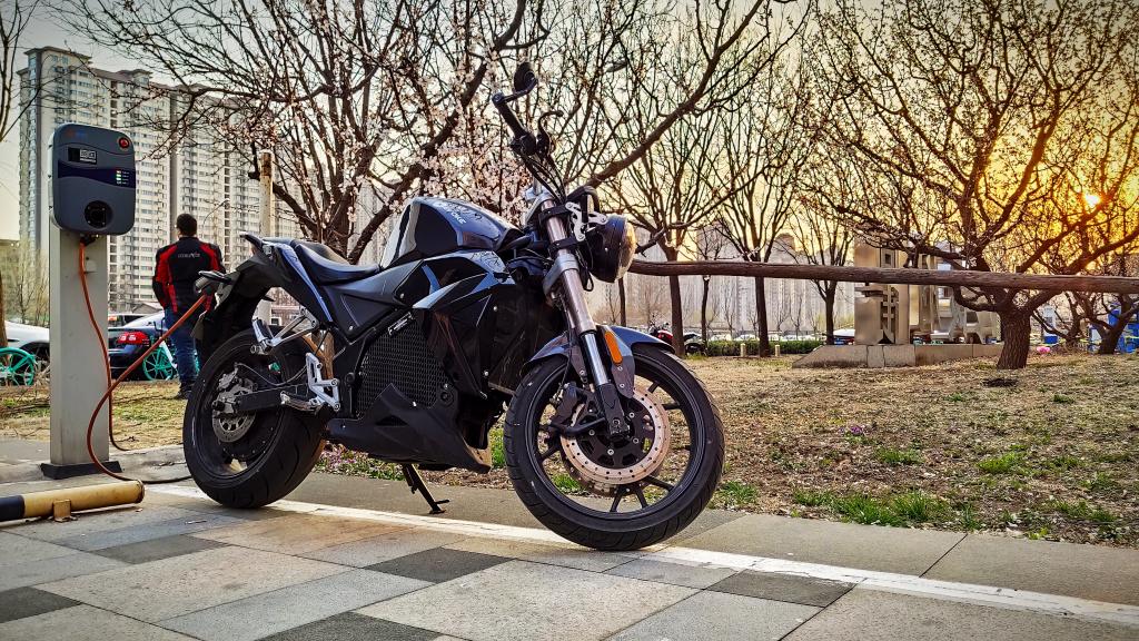 A black electric motorcycle is parked on the sidewalk next to a charging station.