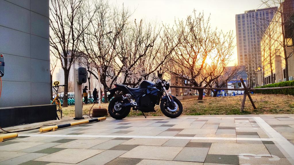 An electric Urban S motorcycle is parked in a parking lot in front of a building.