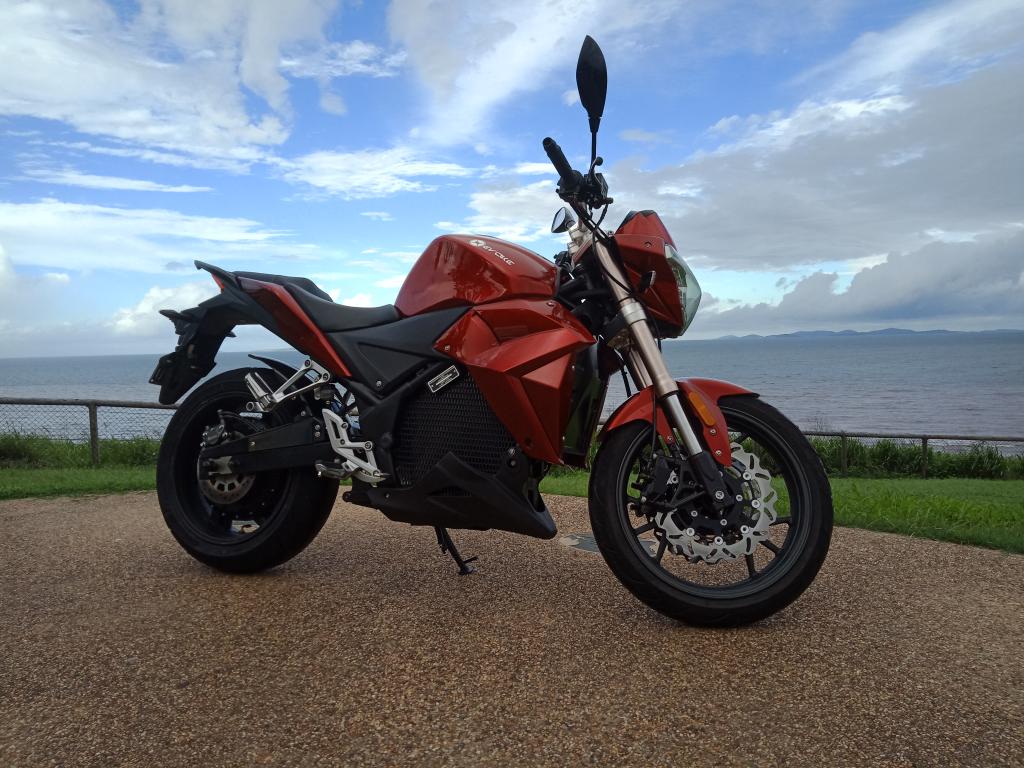 A red motorcycle is parked on the side of the road in front of the ocean.