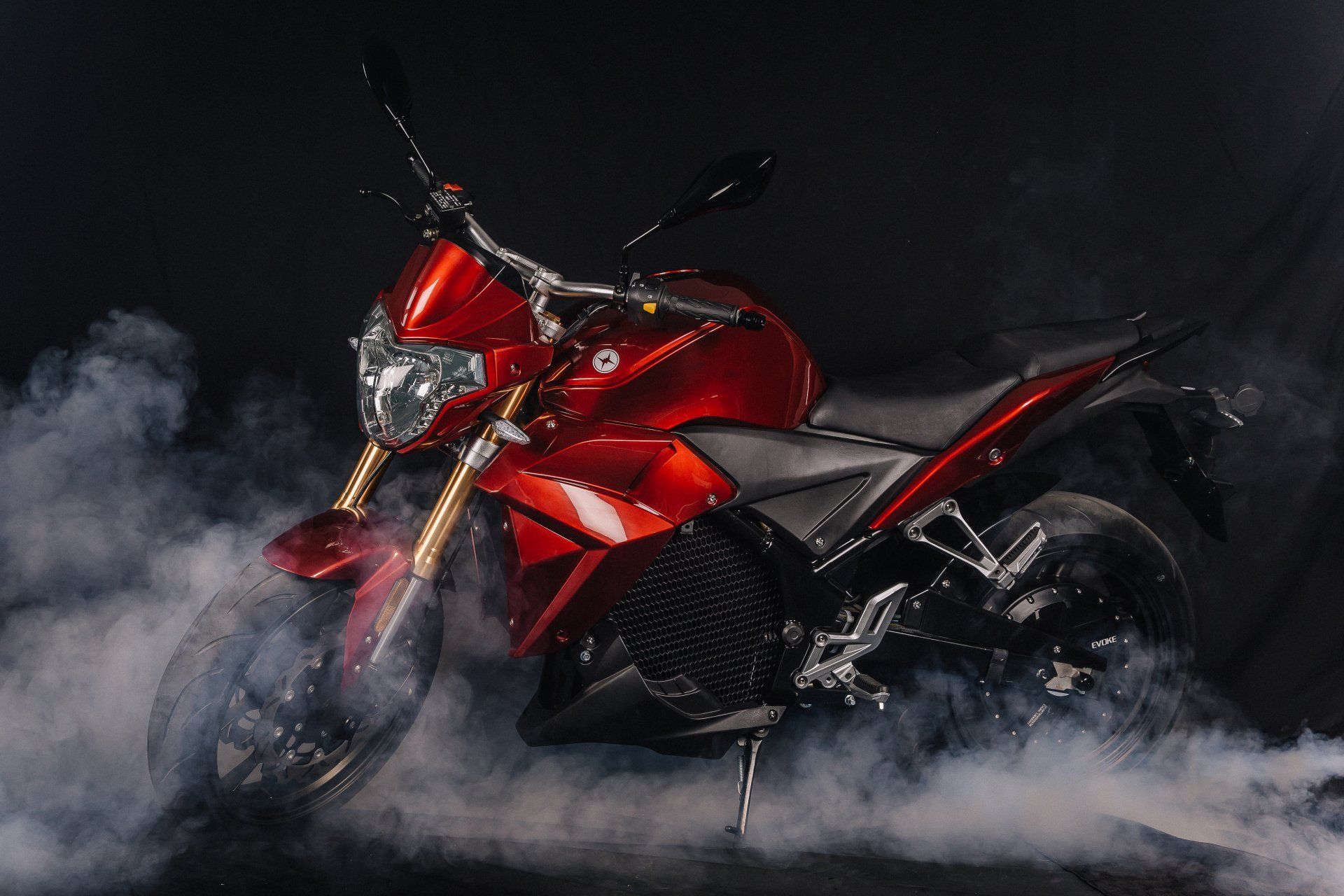 A red Urban S electric motorcycle is surrounded by smoke on a black background.