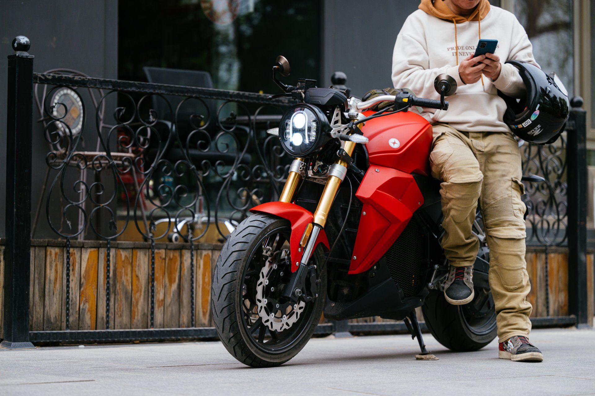 A man is sitting on a red Urban Classic electric motorcycle and looking at his phone.