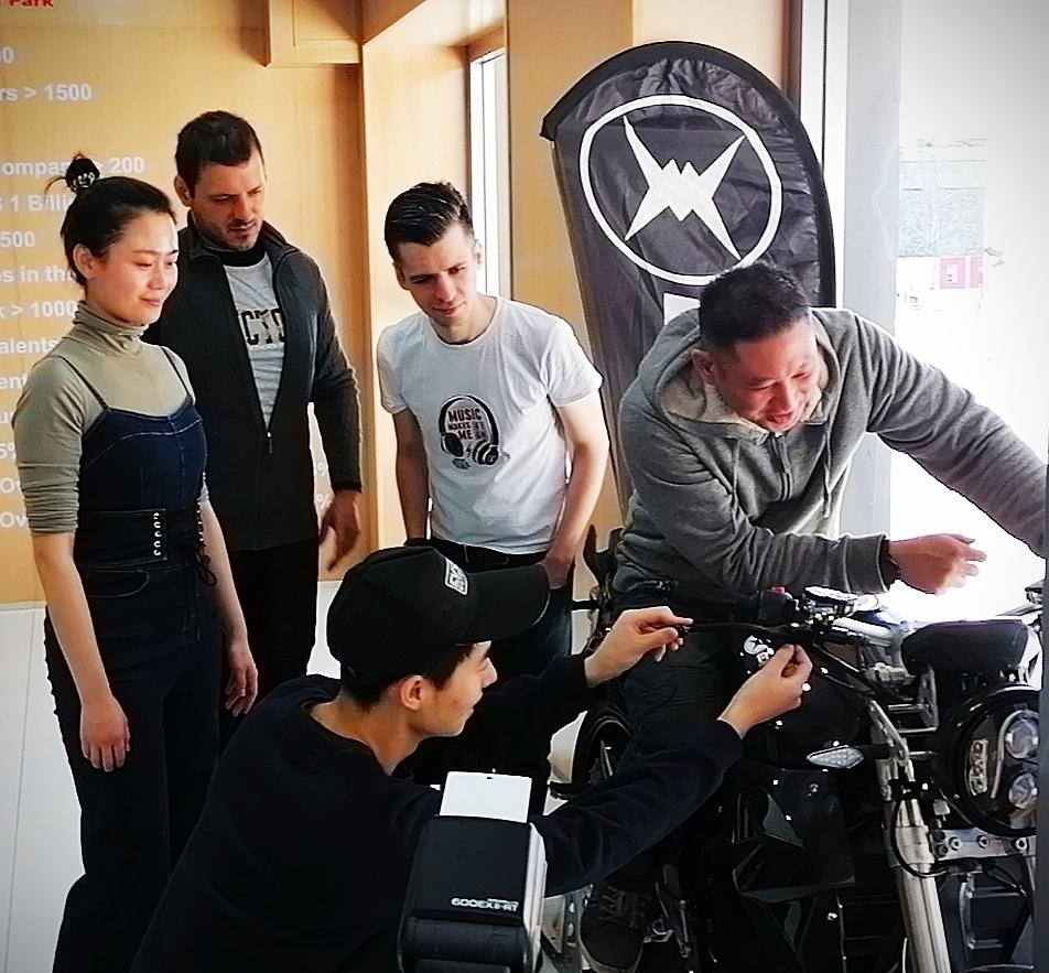 A group of people are working on an electric motorcycle in front of a Evoke Motorcycles logo