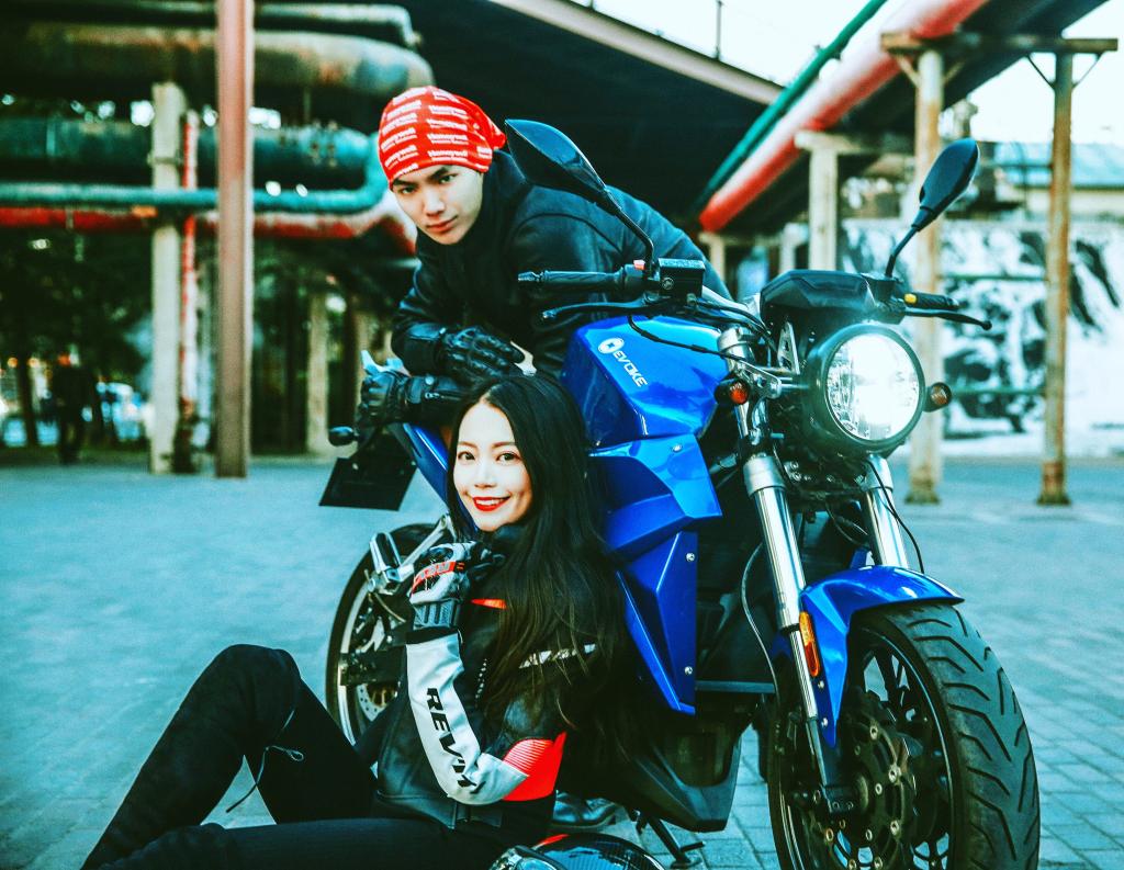 A man and a woman are sitting on an Urban Classic electric motorcycle.