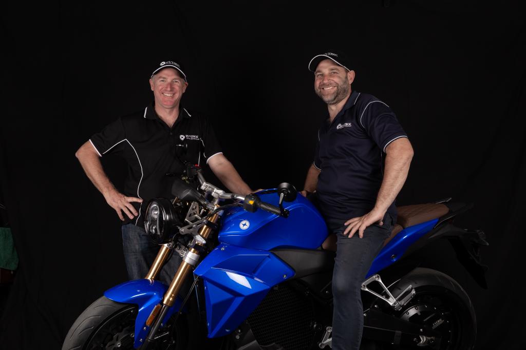 Two men standing next to a blue motorcycle on a black background