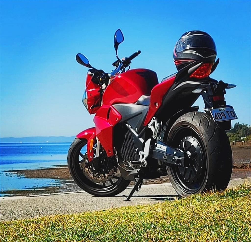 Urban S in red, an electric motorcycle is parked on the side of the road with an ocean in the background