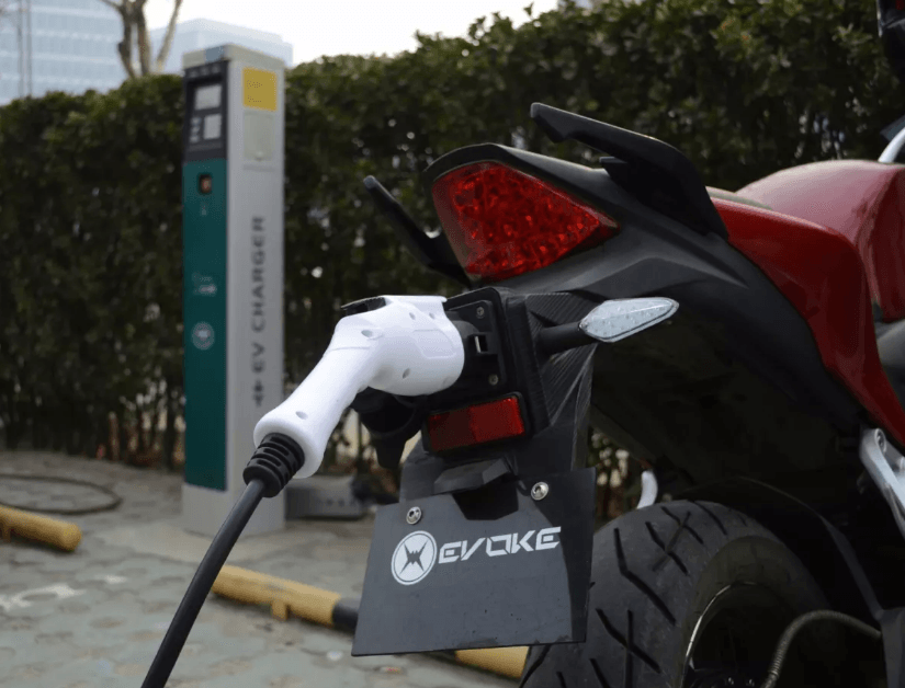 A red electric motorcycle is being charged at an ev charger