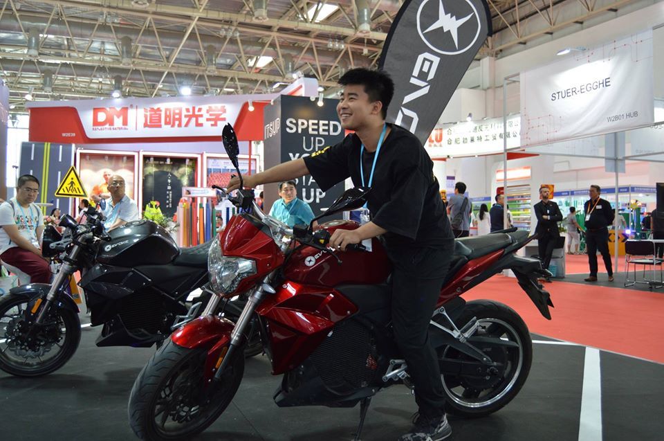 A man is sitting on a red electric motorcycle at a motorcycle show.