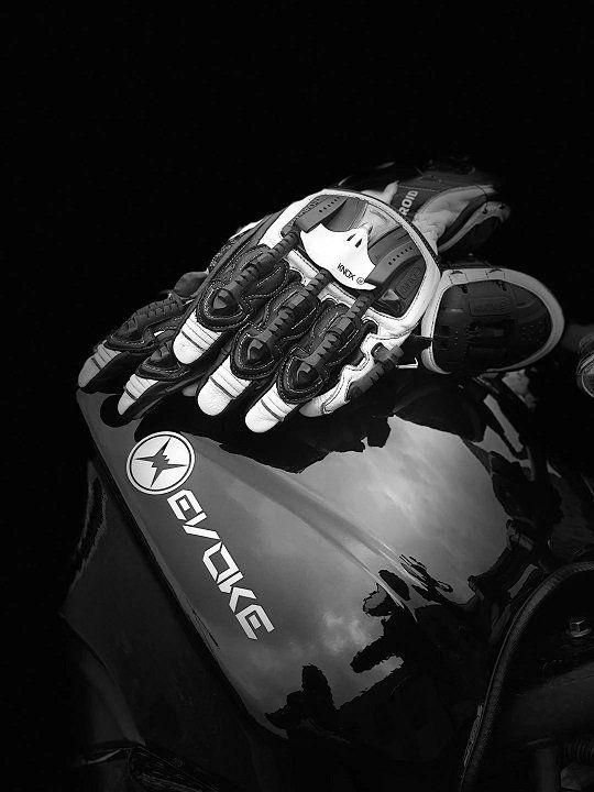 A black and white photo of a pair of gloves on an electric motorcycle.