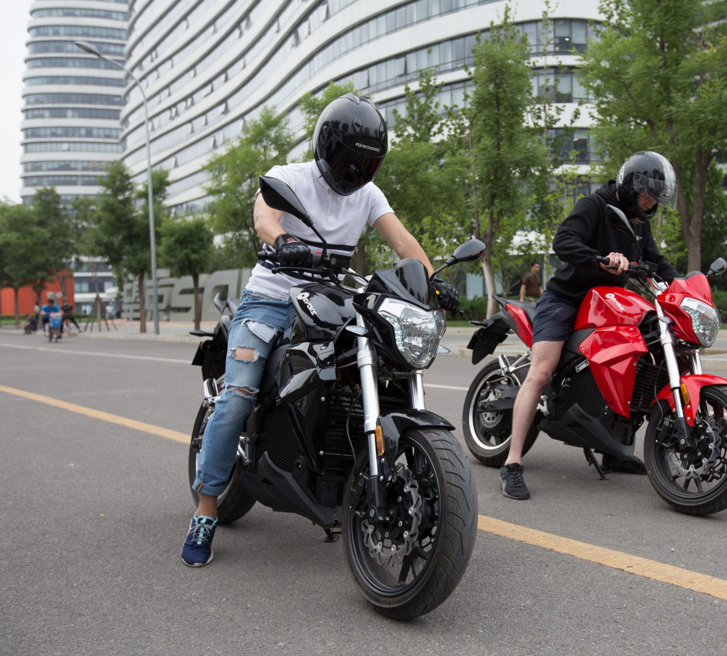 A man in black helmet is riding a black electric motorcycle next to a man in shorts riding a red electric motorcycle. Urban S Beijing, China 2018