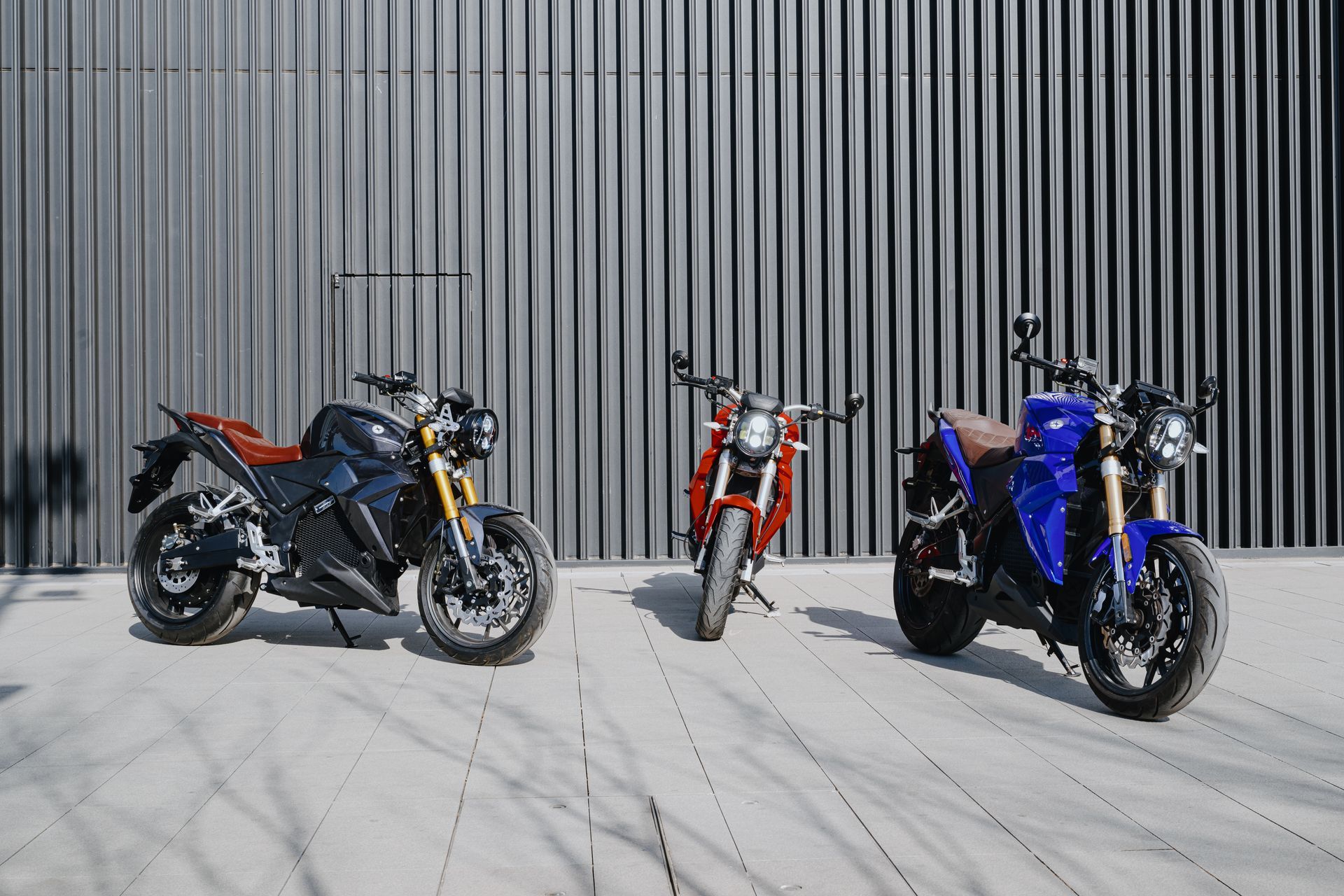 Three Urban Classic electric motorcycles are parked next to each other on a sidewalk in front of a building.