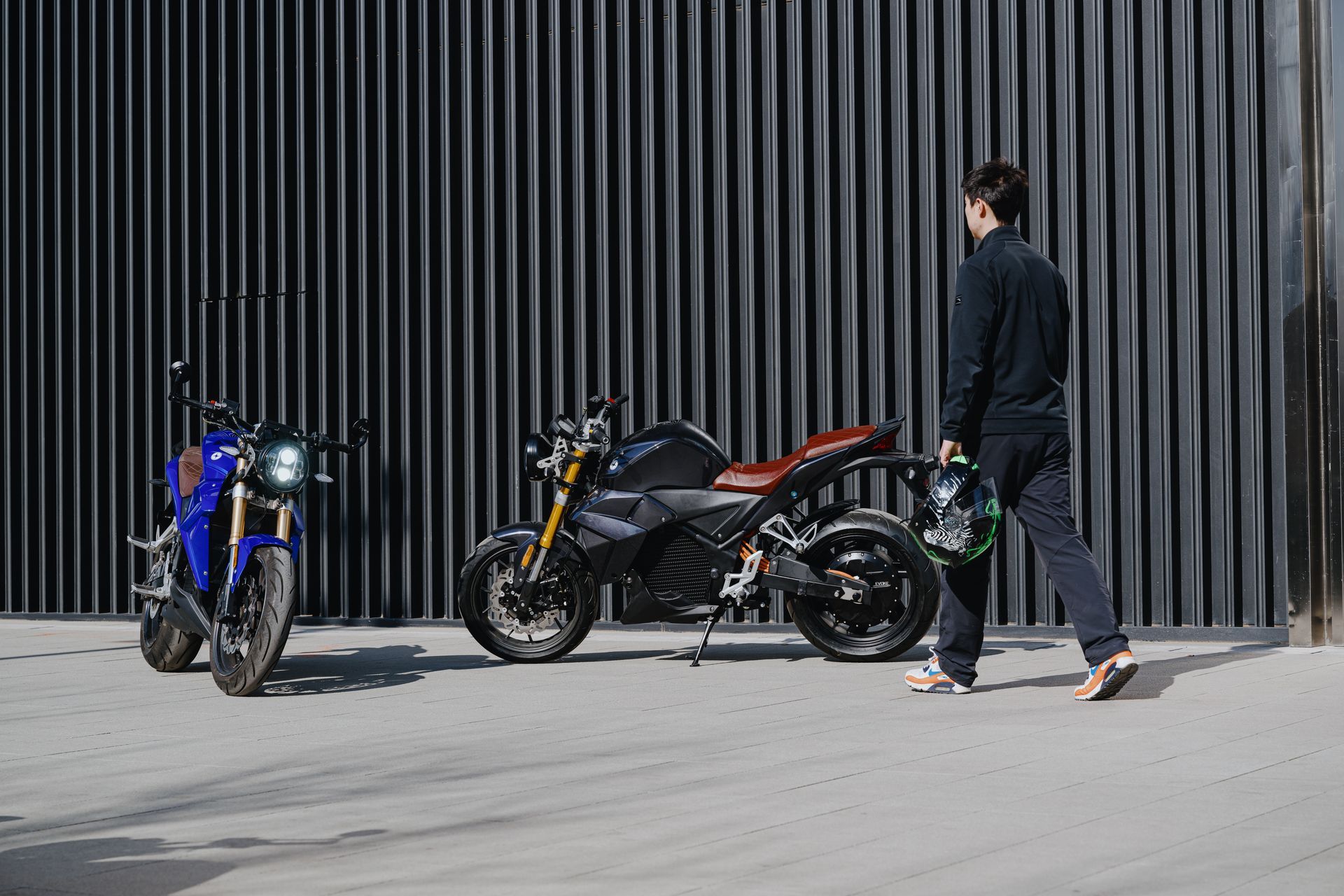 A man is walking past two motorcycles parked in front of a building.