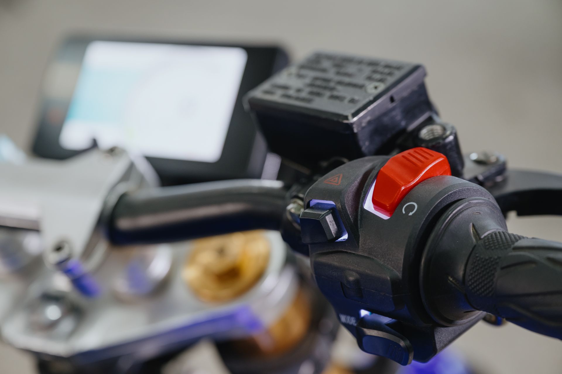 A close up of a motorcycle handlebar with a red button on it.