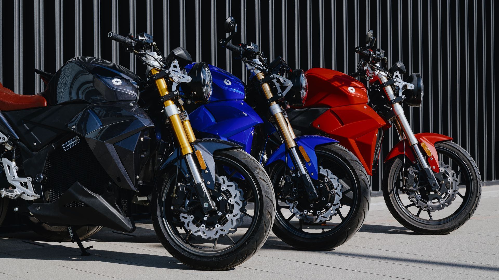 Three urban-classic by evoke_motorycles, electric motorcycles are parked next to each other in front of a fence.
