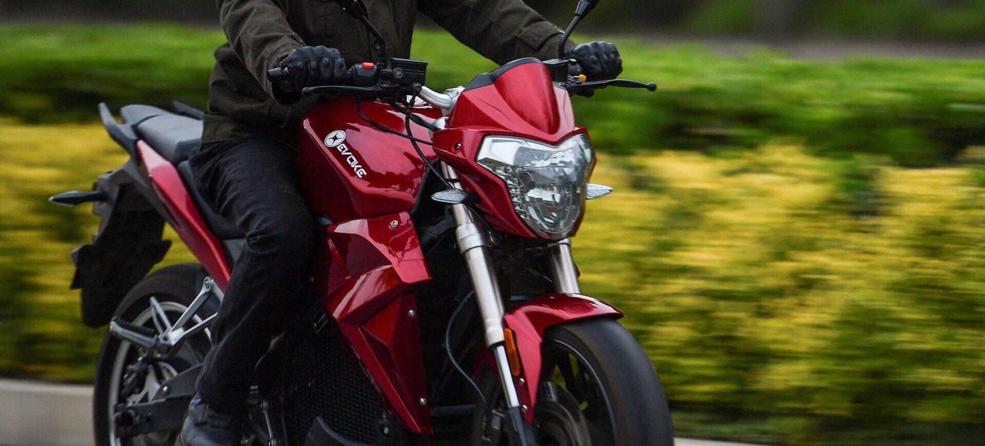 A man is riding a red Urban S electric motorcycle down a road.