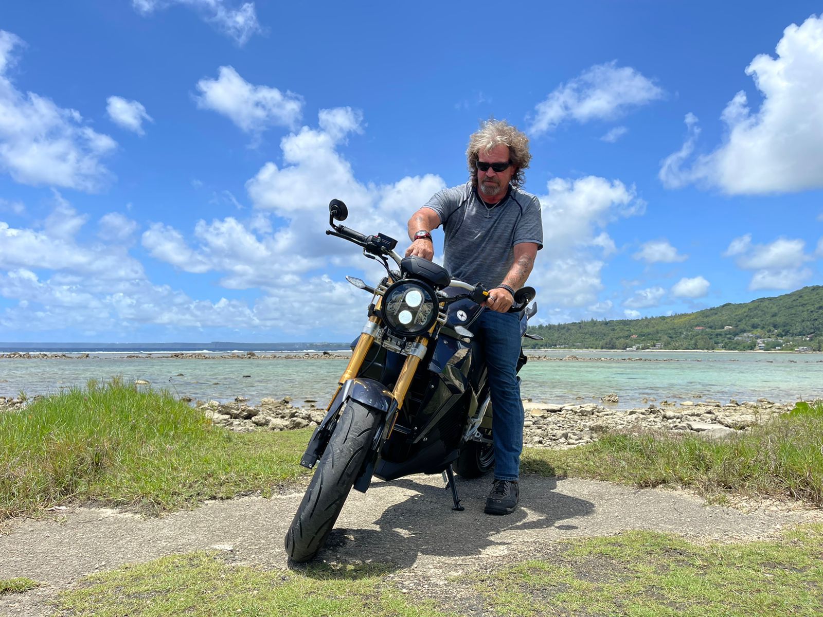 A hot man is sitting on an electric motorcycle near the ocean. Urban Classic 2024 Guam