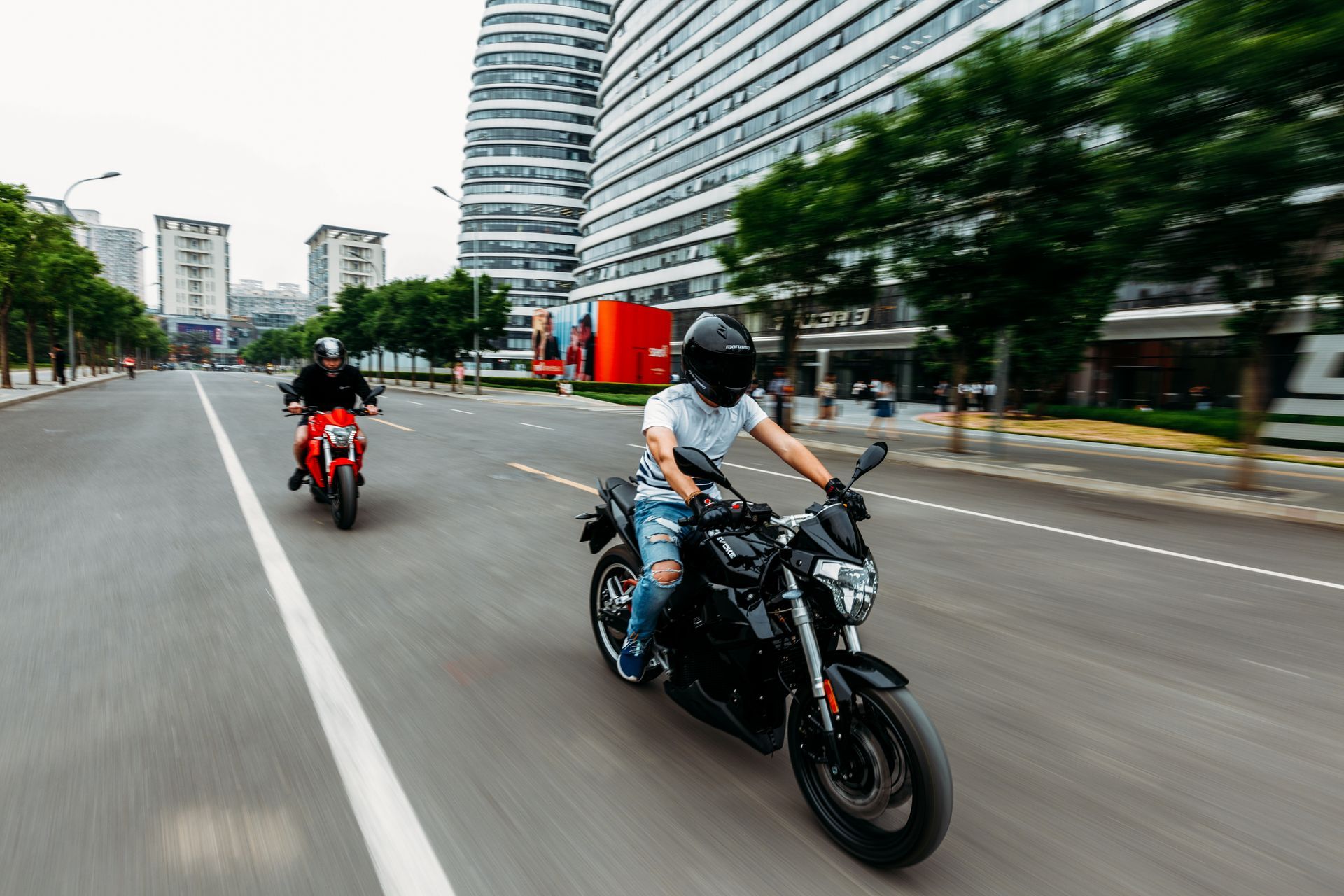 Two people are riding electric motorcycles down a city street.