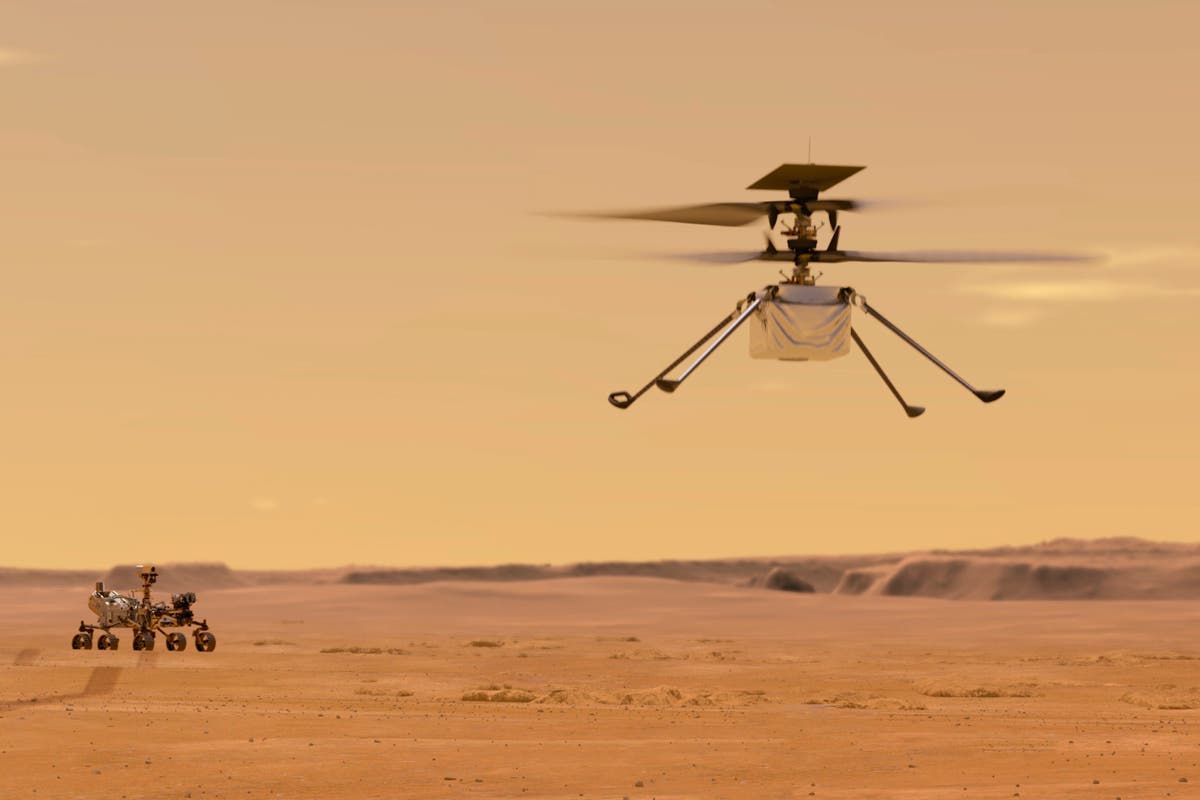 A helicopter is flying over a desert with a rover in the background.
