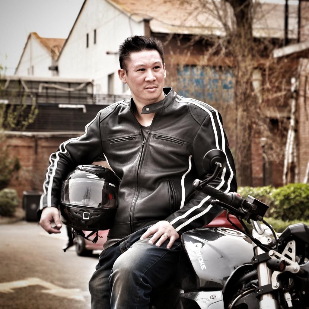 Nathan Siy in a leather jacket is sitting on an electric motorcycle holding a helmet.