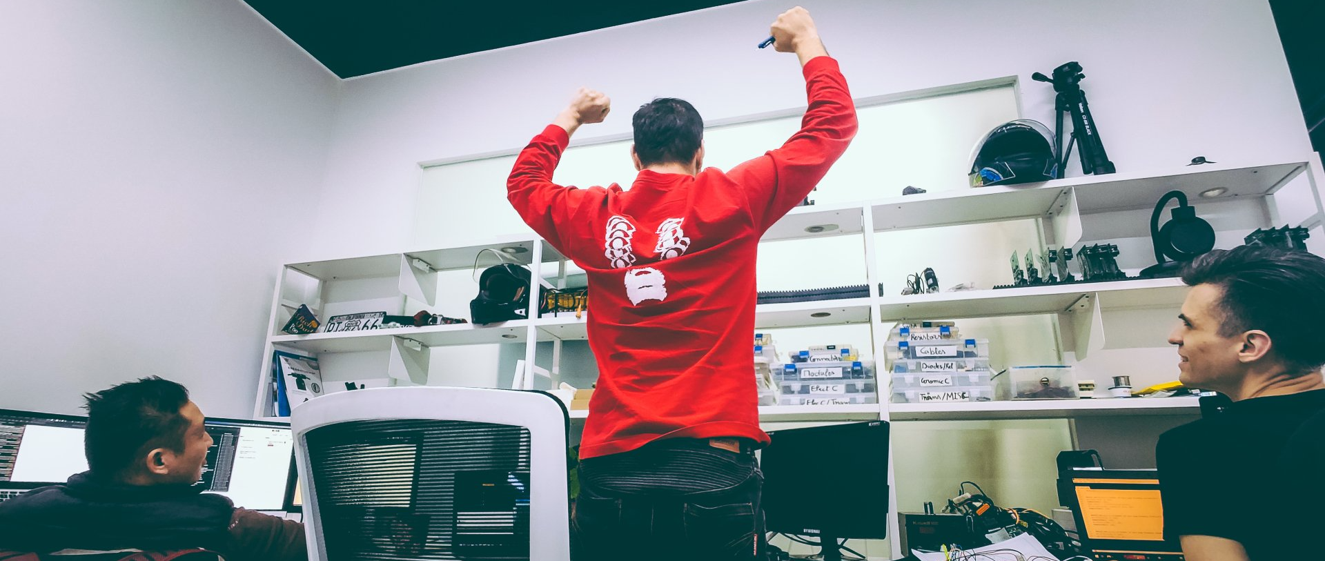 Sebastian Chrobok in a red shirt is standing in a room with his arms in the air celebrating.