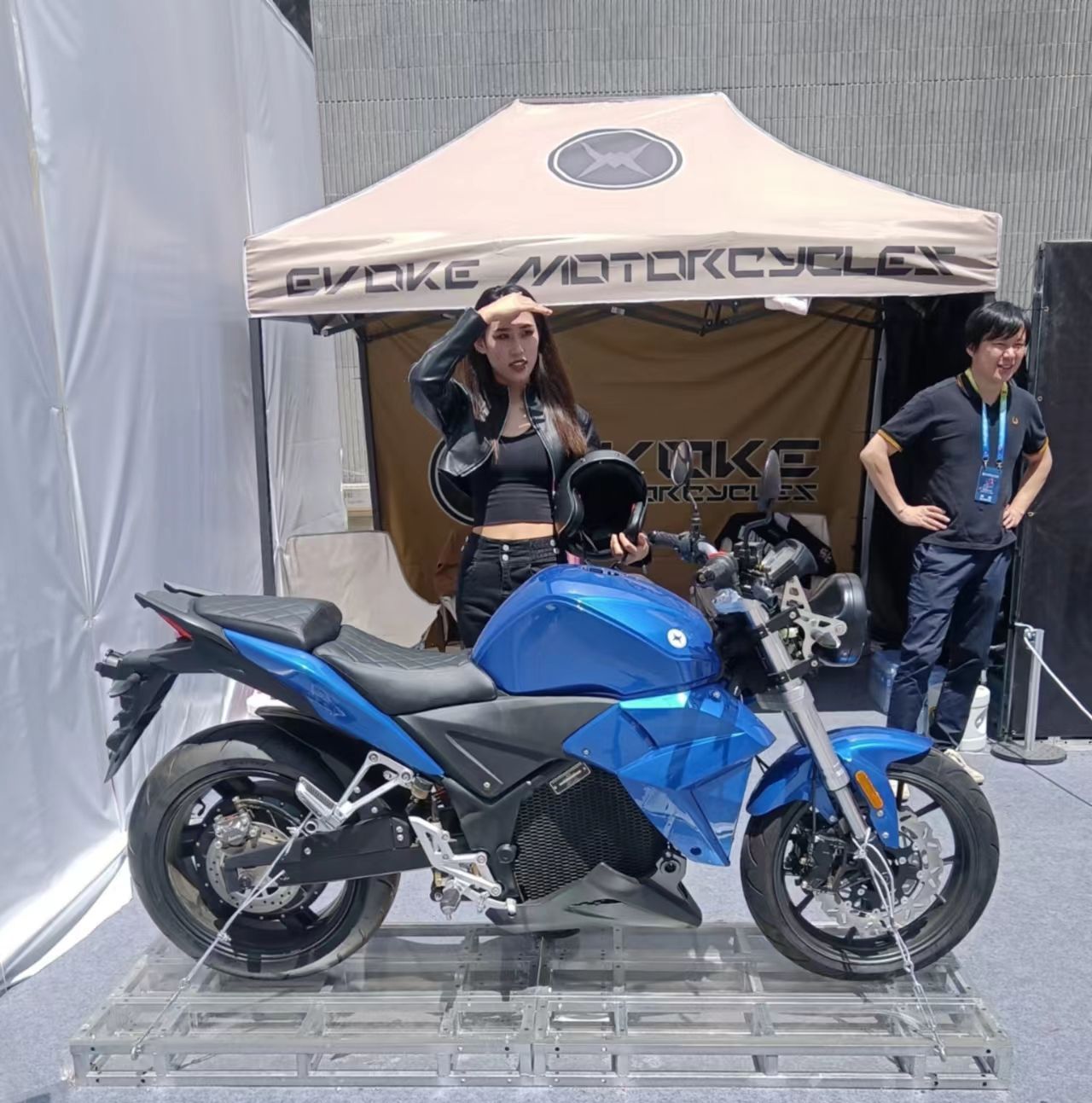 A blue Urban Classic electric motorcycle is parked under a tent that says evoke motorcycles